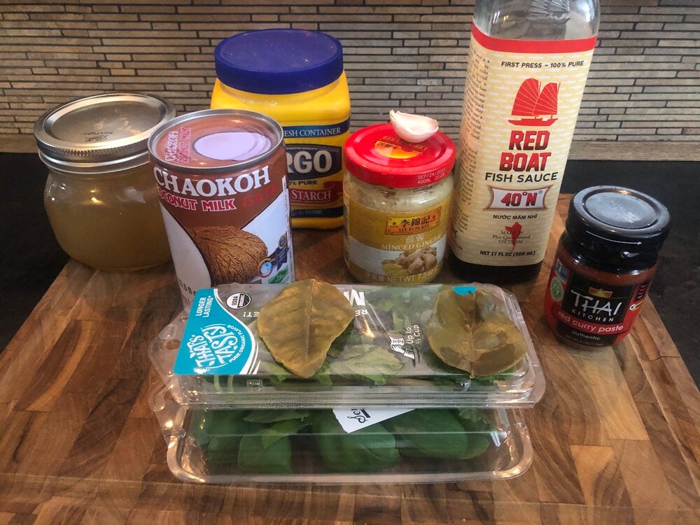 all ingredients for recipe including canned coconut milk, red curry paste, minced ginger, garlic clove, fish sauce, corn starch, basil, mint, and bay leaves
