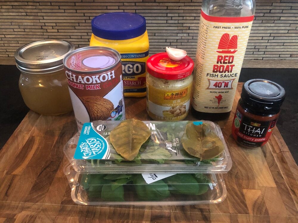 all ingredients for recipe including canned coconut milk, red curry paste, minced ginger, garlic clove, fish sauce, corn starch, basil, mint, and bay leaves