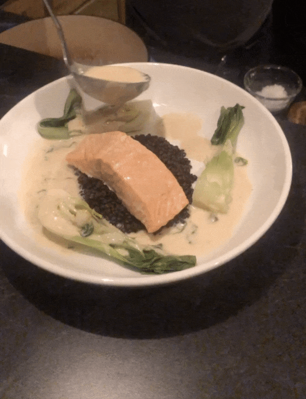 gif of steamed salmon on top of cooked lentils with steamed bok choy with ladding coconut milk sauce over top food